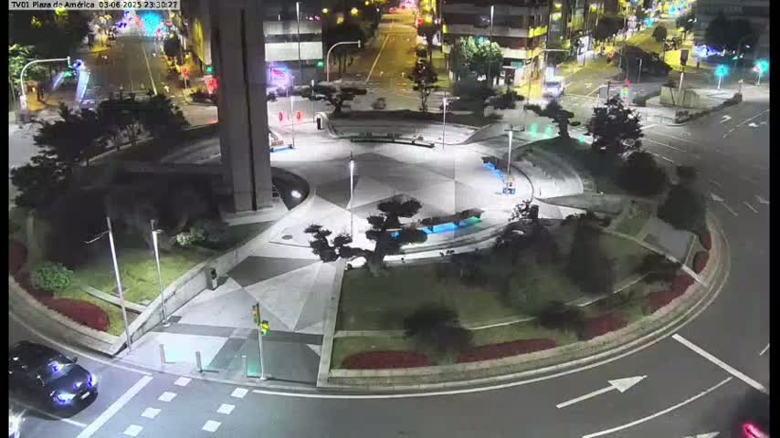 A nighttime aerial view of a roundabout in a city, featuring landscaped areas, lighting, and vehicles on the roads.