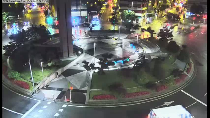 A nighttime aerial view of a geometrically designed roundabout with landscaped areas, illuminated by streetlights, and some vehicles visible on the surrounding roads.