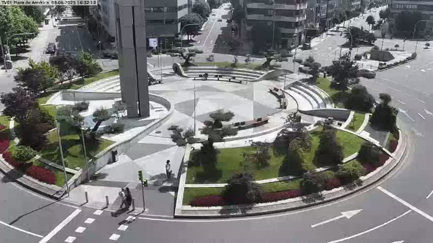 A circular plaza with landscaping and a paved central area is surrounded by a roadway on a sunny day.