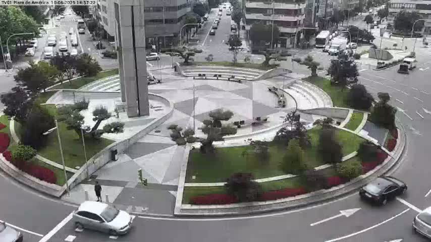An overhead view of a circular plaza with landscaping, benches, and a few cars driving around it on a cloudy day.
