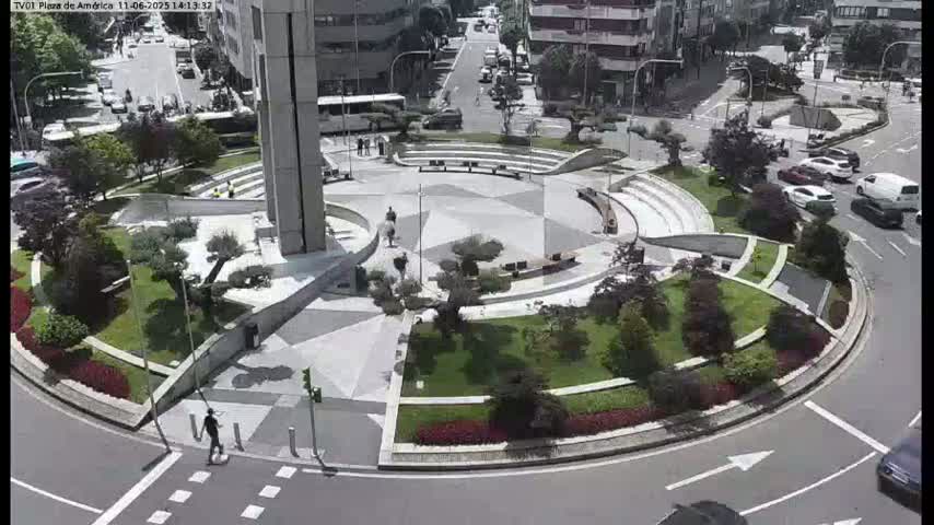 A landscaped traffic circle with a central plaza, surrounded by buildings and cars on a sunny day.