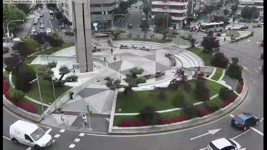 A paved roundabout with landscaped areas and several vehicles is visible from an elevated viewpoint on an overcast day.