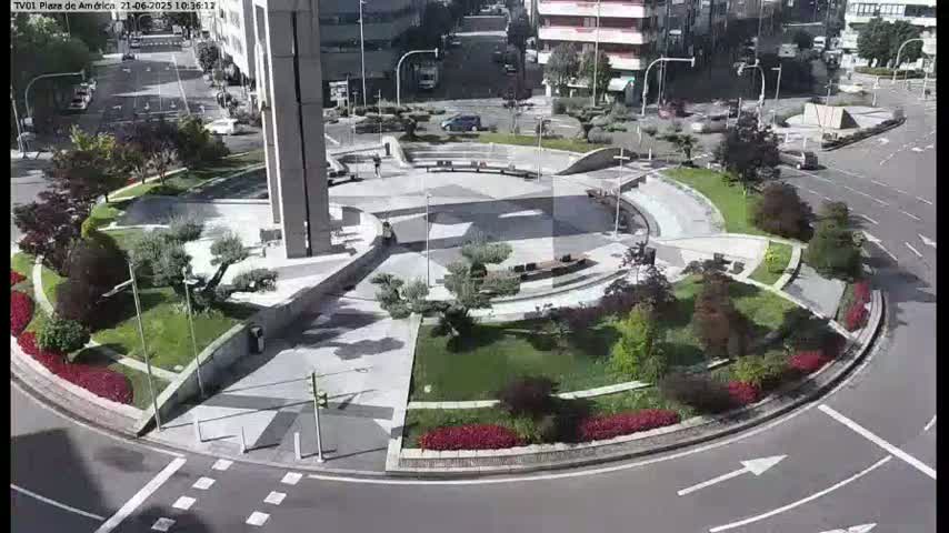 An aerial view of a landscaped traffic circle on a sunny day, featuring a central plaza with benches and greenery surrounding it.