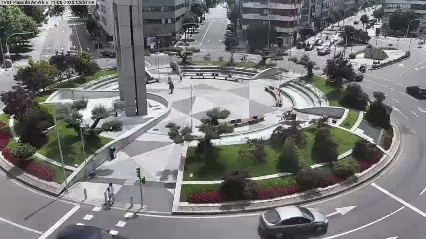 An aerial view of a circular plaza with landscaping and a few pedestrians, surrounded by streets with cars, on a sunny day.