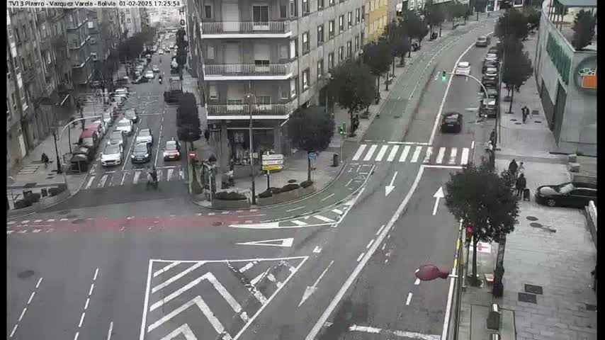 A city street intersection with several cars and pedestrians, under an overcast sky.