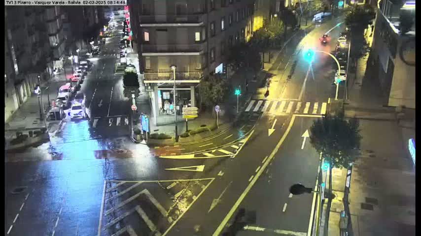 A wet, night-time street intersection with several cars and buildings visible.