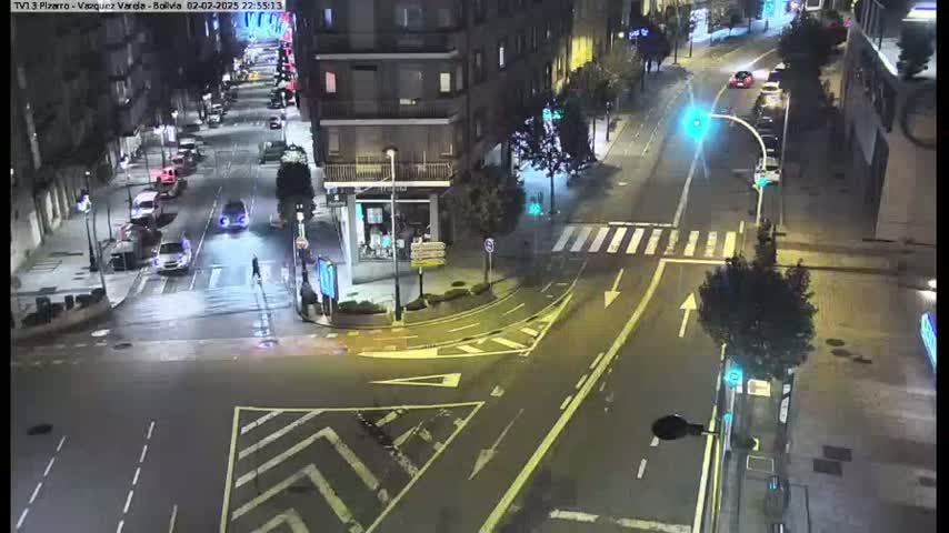 A nighttime, high-angle view shows a city intersection with several cars and pedestrians, under streetlights.