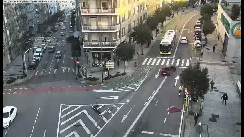 A high-angle view of a city intersection with several cars and a bus, under sunny conditions.