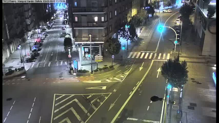 A nighttime street intersection with several cars parked along the sides of the road, illuminated by streetlights.