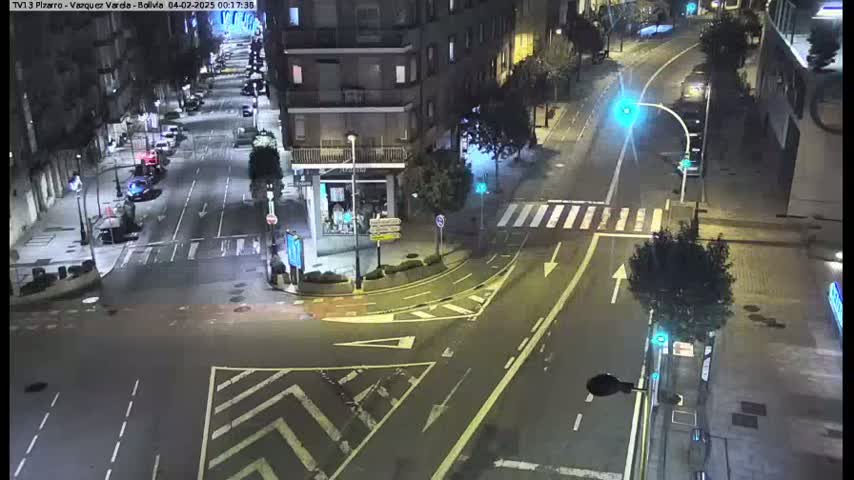 A nighttime aerial view of a city intersection with sparsely trafficked roads and buildings surrounding it.