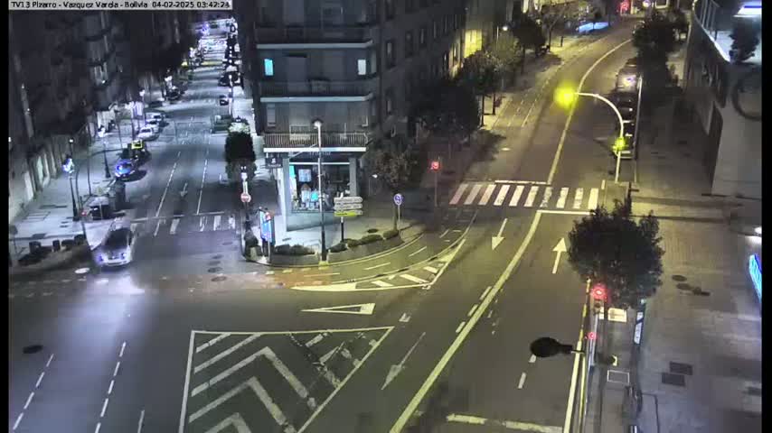 A nighttime high-angle view of a city intersection with several cars and buildings visible under clear skies.