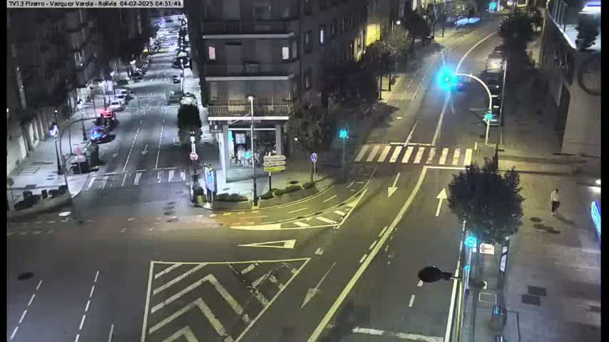 A nighttime street intersection with a few cars and pedestrians, illuminated by streetlights.