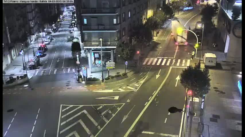 A nighttime, high-angle view of a city intersection with several cars and a few pedestrians.