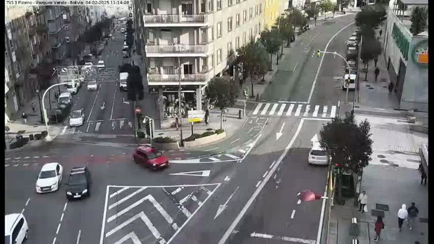 A high-angle view of a city intersection with several cars and pedestrians on a sunny day.