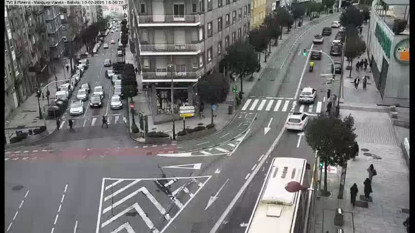 A city intersection with several cars and pedestrians, viewed from above on a cloudy day.