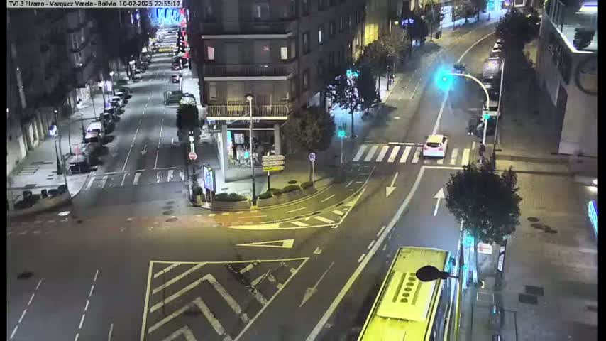 A nighttime aerial view of a city intersection with several cars and a bus, under clear skies.