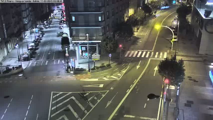 A nighttime aerial view of a mostly empty city intersection with parked cars lining the streets.