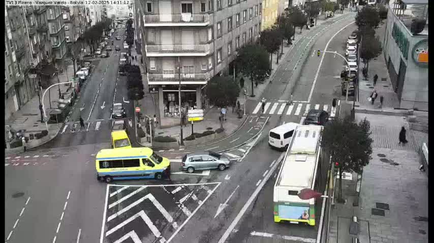 A city street intersection with several vehicles, including a bus and van, is shown on an overcast day.