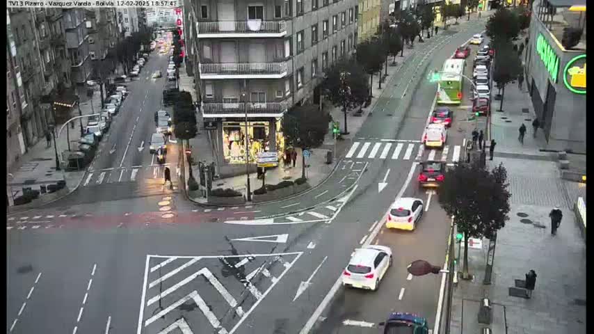 A city intersection with several cars and pedestrians, under overcast daytime conditions.