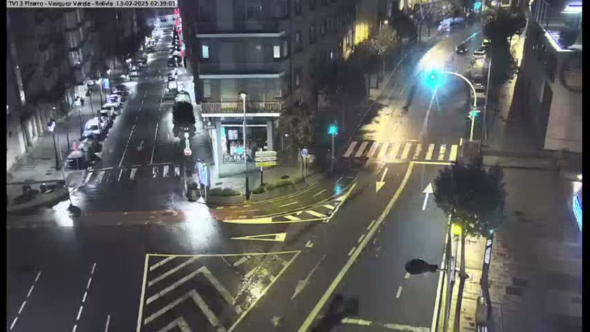 A wet, nighttime street intersection shows several cars and buildings under streetlights.