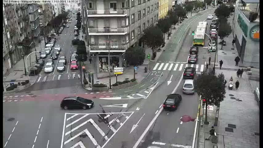 A city intersection with several cars and pedestrians, on an overcast day.