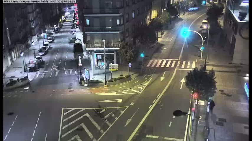 A nighttime, high-angle view of a city intersection with sparsely populated streets, buildings, and traffic signals.