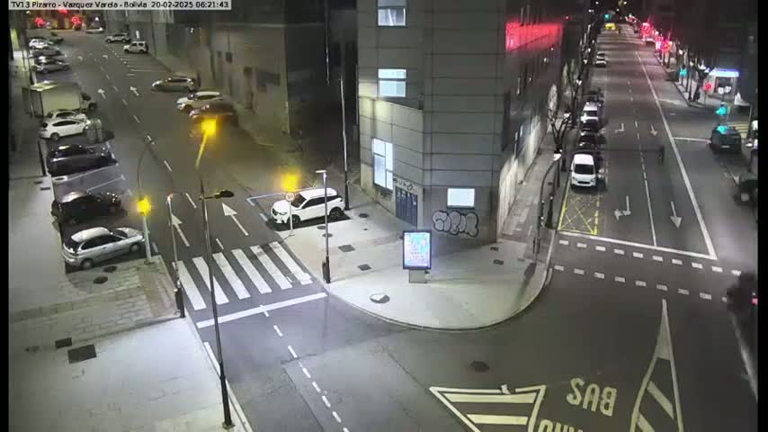 A nighttime street intersection with parked and moving cars under streetlights.