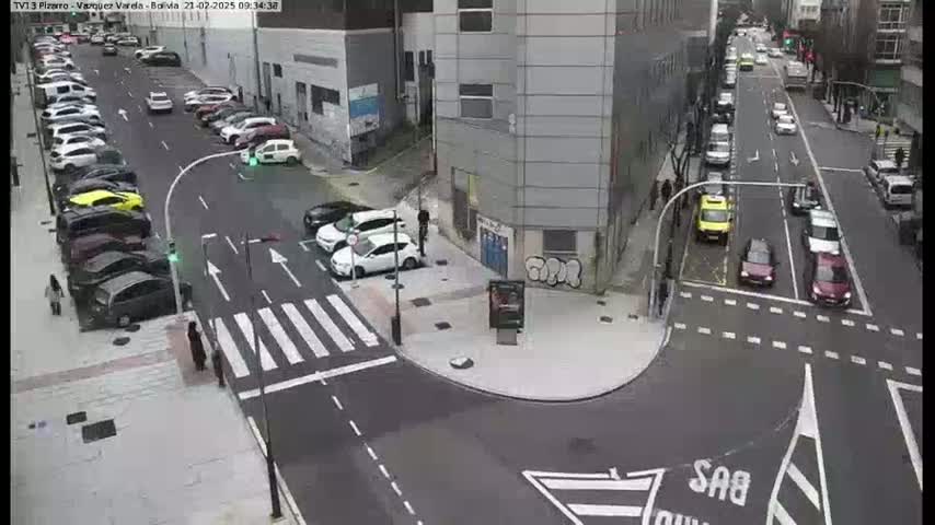 A city street intersection with parked and moving cars on a mostly clear day.