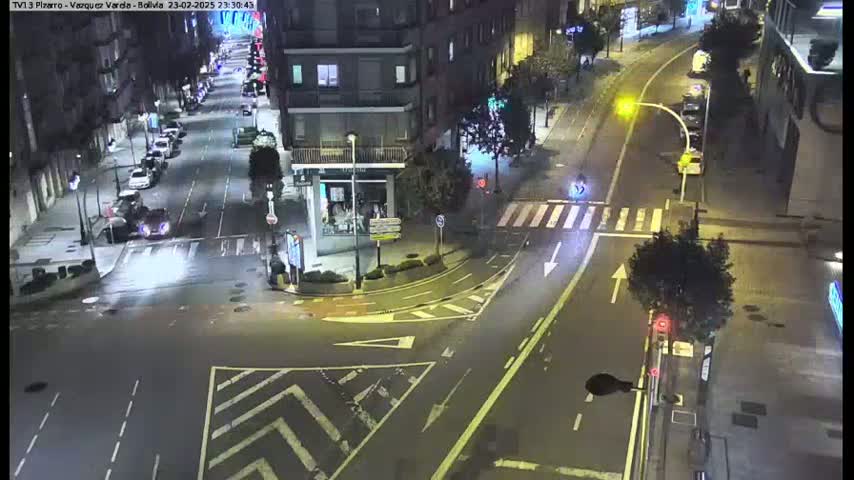 A nighttime aerial view of a city intersection with several cars and a streetlight, under clear skies.