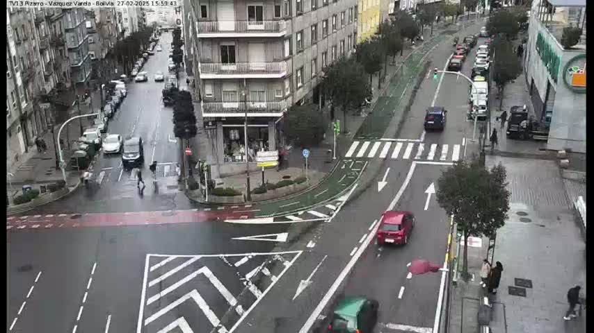 A rainy city street intersection shows several cars and pedestrians, with a bike lane and crosswalks visible.