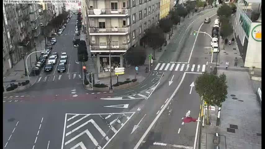 A city intersection with several cars and pedestrians, under a mostly clear sky.