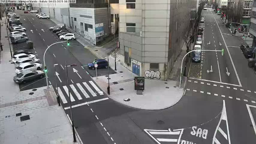 A street intersection with parked cars and several vehicles driving on a mostly clear day.