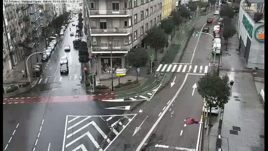 A rainy city street scene shows a multi-lane road with cars and a crosswalk, flanked by buildings and bicycle lanes.