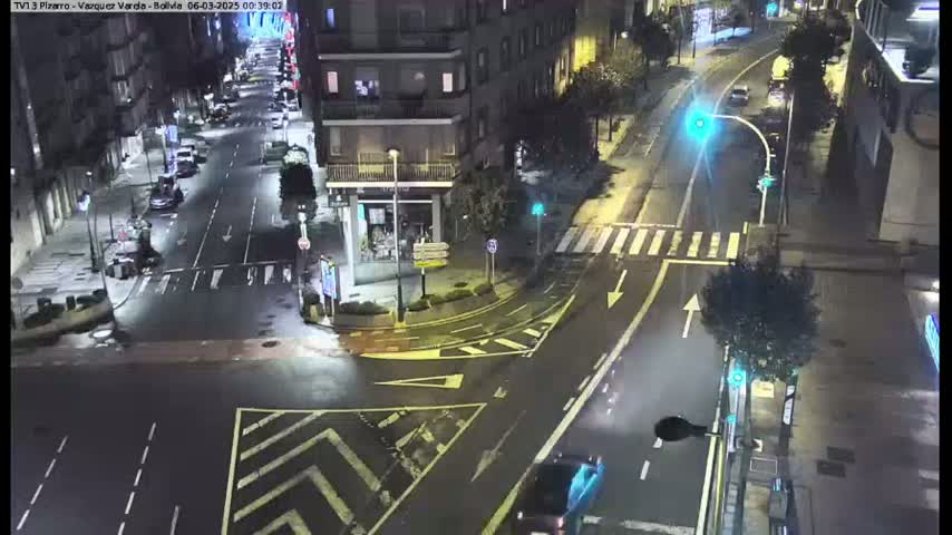 A wet, nighttime street intersection shows several cars and buildings, with some streetlights illuminating the scene.