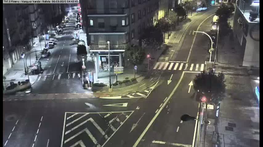 A wet, nighttime street intersection shows several cars and buildings under streetlights.