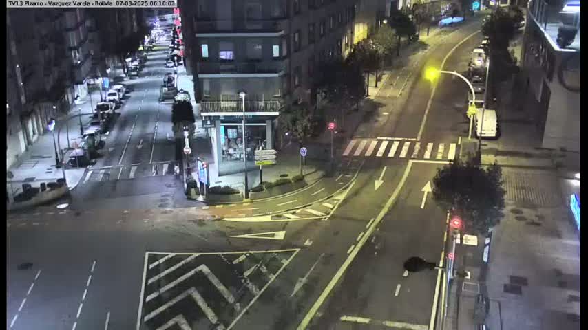 A nighttime aerial view of a city intersection with sparsely parked cars along the sides of the roads.