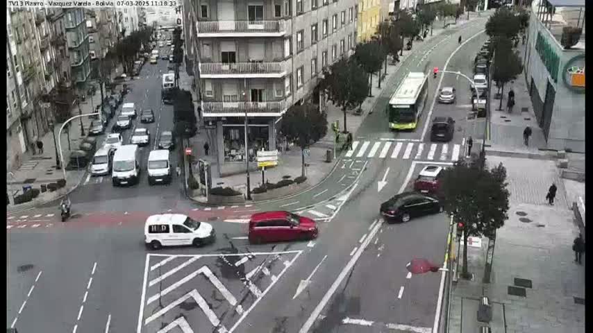 A city intersection with several cars and a bus, under a mostly cloudy sky.