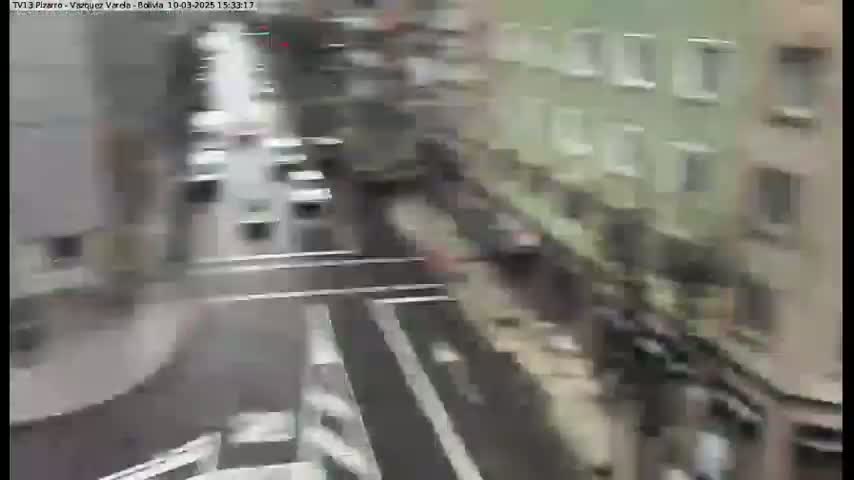 A high-angle, blurry view shows a street scene with vehicles and buildings, possibly on an overcast day.