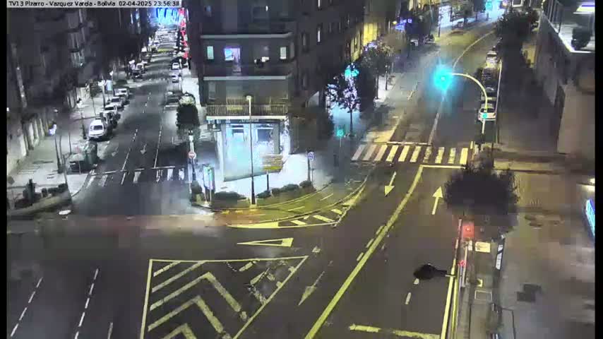 A wet, nighttime street intersection shows several vehicles and buildings under streetlights.