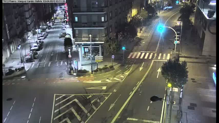 A nighttime aerial view shows a city intersection with several cars and buildings, under clear skies.