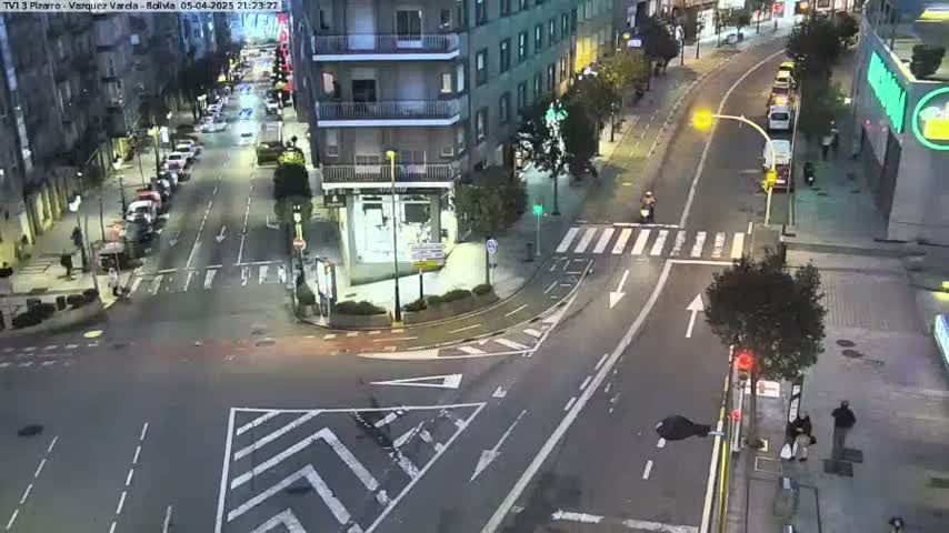 A nighttime street intersection with parked cars and a few pedestrians, under clear skies.
