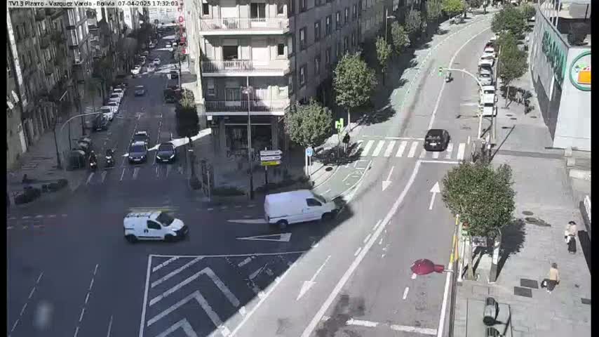 A sunny day shows a city intersection with several cars and pedestrians, and a white van is turning right onto a cross street.