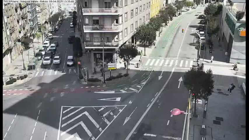 A sunny day overhead shows a city intersection with several cars and pedestrians, including a bike lane.