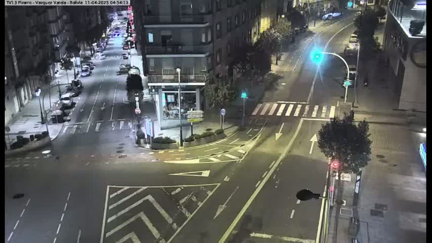 A nighttime, high-angle view of a mostly empty city intersection with cars parked along the sides of the streets.