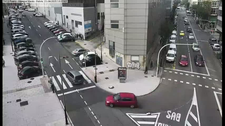 A street intersection with parked cars and several cars driving on a sunny day.