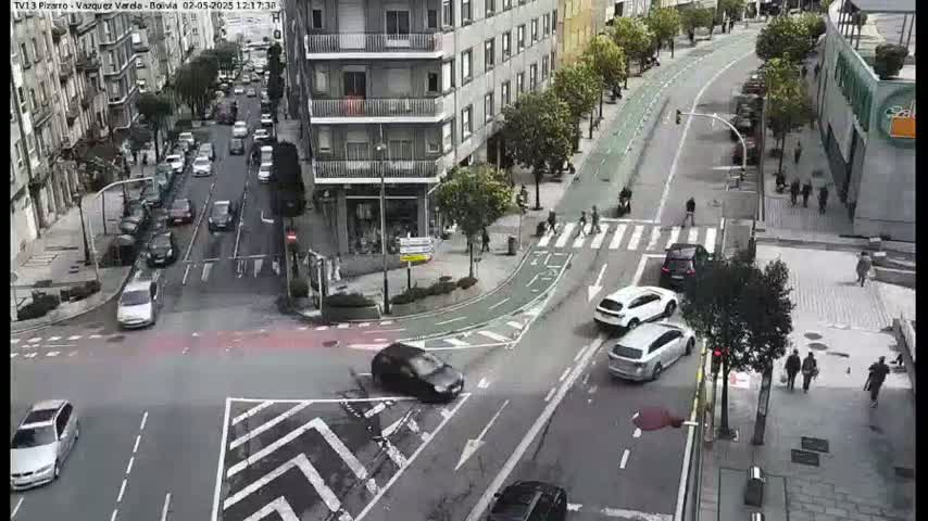 A city street intersection with cars and pedestrians, under a mostly cloudy sky.