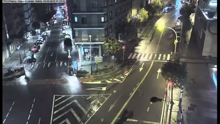 A wet, nighttime street intersection shows several cars and buildings under dim streetlights.