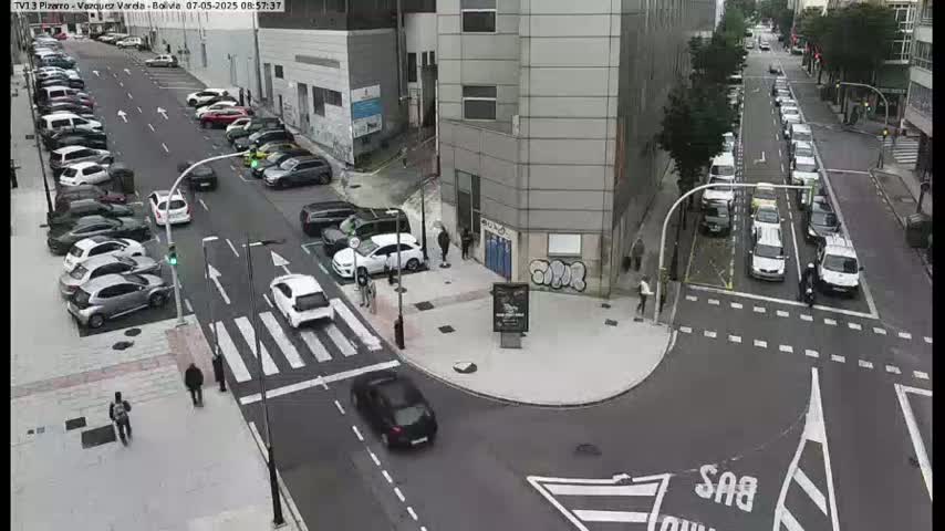 A high-angle view of a city intersection with parked and moving cars, pedestrians, and a building with graffiti.