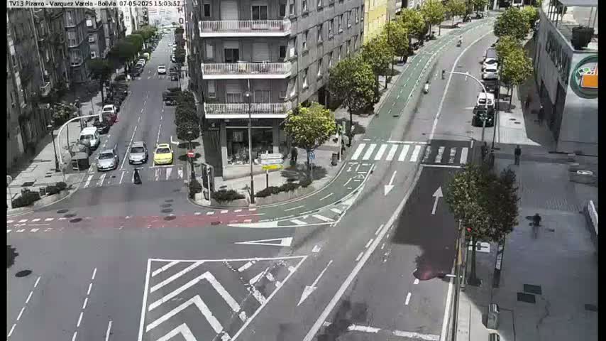 A sunny city street intersection shows several cars stopped at a crosswalk, with a bike lane curving around the corner.