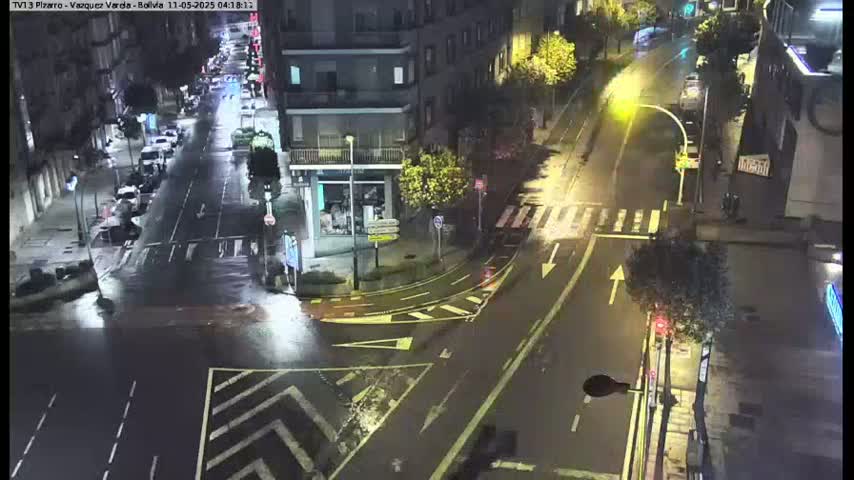 A rain-slicked street intersection at night shows several cars and buildings under streetlights.